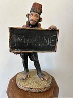 Front view of the monkey figurine holding advertising chalkboard sign with 'IMAGINE' written on it
