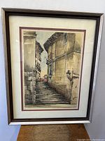 Frontal image of the framed watercolor painting showing the street scene with stone stairs and textured buildings, with visible artist signature.