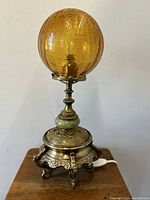 Front view of the gothic style brass table lamp with amber crackle glass globe shade on a wooden surface.