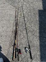 Four vintage fishing rods with reels laid on asphalt, showing different styles of handles and reels.