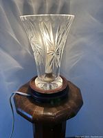 Full view of the crystal trumpet-shaped lamp lit on wooden octagonal base showing pin-wheel cut starburst pattern and cord.