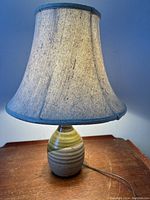 Angled view of the mid-century modern pottery lamp lit showing the fabric shade and colors of the base.