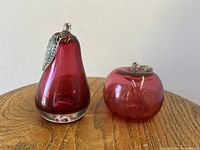 Pair of Mid Century Murano Italy cranberry blown glass sculptures, pear and apple shapes with silver glass leaves, shown together on a wooden surface.