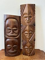Pair of vintage carved wood African tribal head wall hangings shown together standing side-by-side against a white wall.