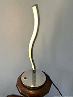 Front view of the silvered metal LED spiral desk lamp showing the curved LED light and chromed round base with power button.