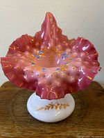 Front view showing ruffled cranberry top with gold and blue hand-painted decoration and white glass base.