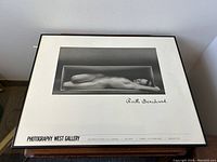 Framed black and white photo of nude woman lying in a rectangular box, matted with white border and signed by Ruth Bernhardt.