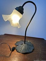 Full view of the vintage lily pad table lamp illuminated showing frosted art glass ruffled shade and curved stem.