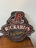 Frontal close-up of the Rickard's sign showing red, white, and black colors with chain on sides.