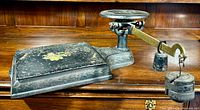 Antique cast-iron balance scale resting on a wooden surface, showing floral decoration and attached weights.