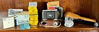 Group photo of vintage Balda Baldinette camera, leather case, boxes of Kodak filters, film rolls, and other camera accessories on wood background.