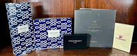 Five boxed designer accessories grouped on wood table, visible brands include Estee Lauder, Yves Saint Laurent, Sisley Paris, and Swarovski.