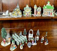 Full set view showing four village buildings on top shelf, multiple figurines, trees, benches, and lamp posts on bottom shelf