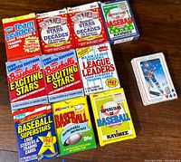 Photo showing a collection of 14 packs of vintage baseball trading cards and stickers from various brands including Fleer, Kmart Topps, Kay-Bee, and Playoff alongside a small stack of Mike Bossy hockey cards on the right.