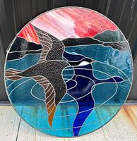 Full view of the round stained glass panel with colorful depiction of Canadian geese flying over a lake and mountains with a red sky.