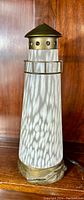 Front view of the lighthouse lamp showing the art glass body with bronze base and brass railing