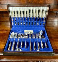 Complete flatware set displayed in original wooden tarnish-proof chest with blue velvet lining, showing all pieces organized in slots.