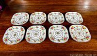 Eight square Royal Albert Petit Point bone china plates arranged in two rows on a wooden surface.