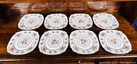 Eight Royal Albert Petite Point bone china dinner plates arranged in two rows of four on a wooden surface.