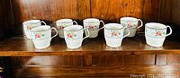 Eight Royal Albert Petit Point coffee mugs arranged on a wooden shelf.