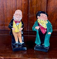 Two Royal Doulton Charles Dickens bone china figurines, full view on wooden surface