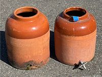 Two vintage pottery jugs outdoors on pavement. One jug missing spout, both show wear and aging.
