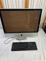 Front view of Apple iMac 24 inch computer and wired keyboard on white surface. Screen is off, showing reflections.