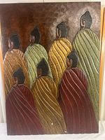 Full view of carved wood wall hanging showing seven spiritual figures with robes in shades of green, yellow and red against a textured brown background.