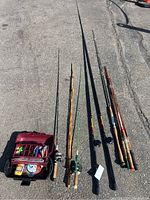 Photo showing seven fishing poles laid out on the pavement, with the longest measuring approximately 12 feet and the shortest about 5 feet. The poles have varied grips including cork and plastic.