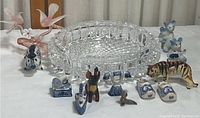 Photo of glass and porcelain animal figurines arranged around a German Crystal dish on a white cloth background.