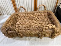 Full view of large rectangular hand woven basket showing two handles and woven flattened base.