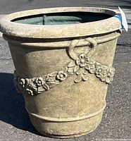 Full view of large circular composite planter with floral garland decoration around its exterior. Shows overall condition and size.