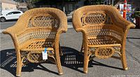 Pair of ornate rattan and wicker outdoor chairs shown side by side in sunlight, highlighting natural tan color and overall structure.
