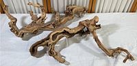 Two irregularly shaped artistic driftwood pieces laid on white fabric, showing twisted, natural wood with knots and holes.
