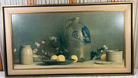 Full view of vintage framed still life print showing porcelain jugs, plate with fruit, and floral accents against a greenish background.