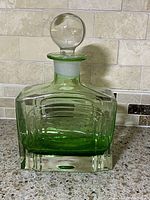 Front view of green transparent Art Deco glass decanter with round stopper on kitchen countertop.