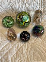 All six paperweights shown on quilted fabric surface, assorted colors and designs visible.