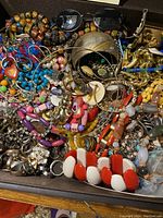 Overview of mixed jewelry collection in a box showing colorful beaded bracelets, rings, necklaces, and metal bangles.