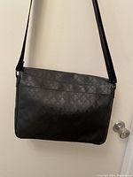 Front view of black messenger bag with embossed fleur-de-lis pattern and shoulder strap.