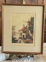 Full view of framed vintage etching depicting stone house with orange roof and turret surrounded by trees.
