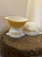 Three vintage Pyrex nesting bowls with floral patterns shown stacked and arranged on a wooden stump surface.