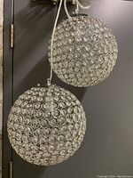 Two spherical pendant lights made of chrome metal frames with circular crystal-like accents, hanging against a dark door.