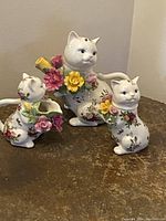 Photo showing three white ceramic cat figurines decorated with colorful hand-painted flowers on table