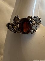 Close-up showing the deep red garnet with detailed floral and leaf accents around the stone in the 10k white gold ring.