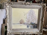 Frontal image of vintage landscape painting in ornate cream-colored frame.