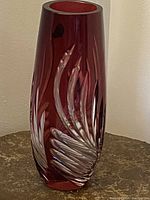 Full view of tall ruby red glass vase showing art deco cut to clear feather and geometric pattern design on cylindrical body.