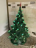 Front view of vintage green ceramic Christmas tree with lit green bulbs and red star topper.