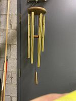 Full view of vintage copper wind chime with wooden top and bottom parts hung against a gray door.