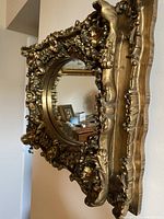Front view of round mirror showing ornate gold leaf frame and convex glass reflection.