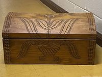 Front view of the wooden trunk showing hand carved flower design on the front panel and top.
